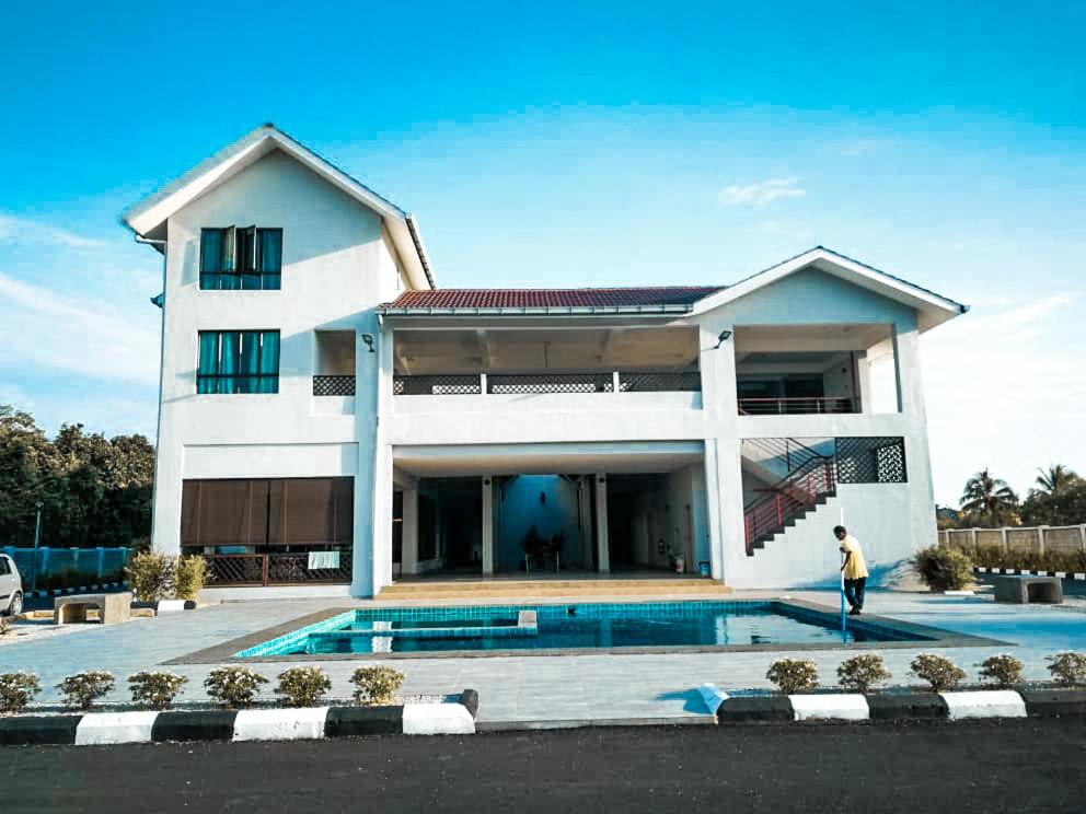 Ein Mann steht vor einem Haus mit Pool. in der Unterkunft KSB Village Resort in Kampong Tambak