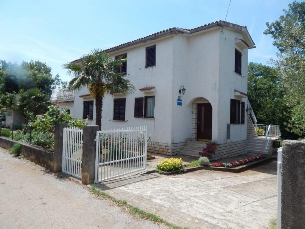 a white house with a gate and a palm tree at Apartman Svjetličić in Brzac