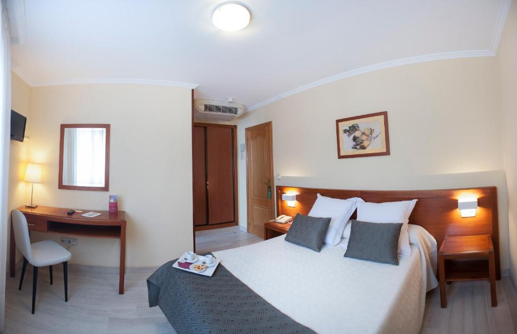 サンティアゴ・デ・コンポステーラにあるホテル サン ロレンツォのベッドとデスクが備わるホテルルームです。