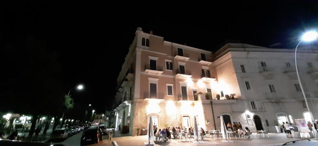 un grand bâtiment avec des personnes debout à l'extérieur la nuit dans l'établissement Palace B&B, à Acquaviva delle Fonti