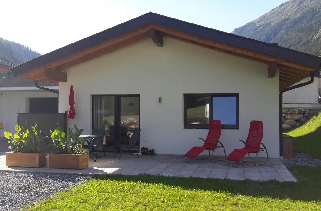 une maison avec 2 chaises rouges et une terrasse dans l'établissement Alpenchalet Pitztal, à Sankt Leonhard im Pitztal