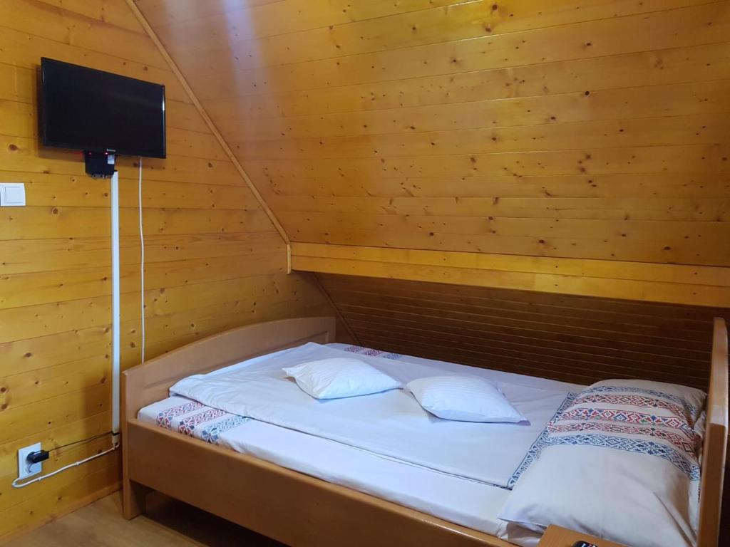 a small bed in a wooden room with a television at Cabana Corbu in Beclean