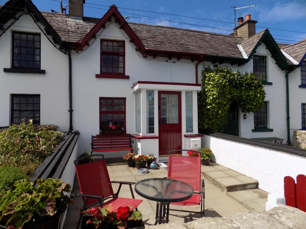 Casa blanca con sillas rojas y mesa en Widows Row Cottage, en Newcastle