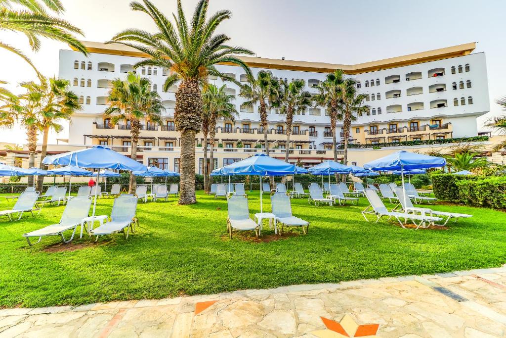 grupa krzeseł i niebieskich parasoli przed hotelem w obiekcie Creta Star Hotel - Adults Only w mieście Skaleta