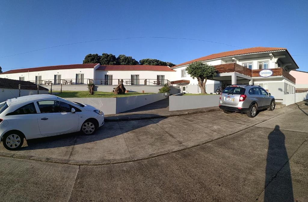 dos autos estacionados en un estacionamiento frente a una casa en Hotel Comodoro, en Corvo