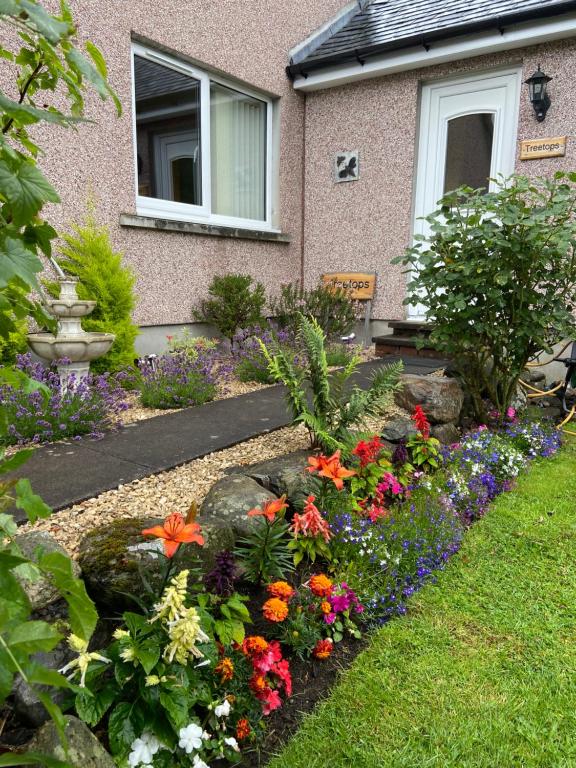 a garden with colorful flowers in front of a house at Treetops Bungalow Loch Ness in Drumnadrochit