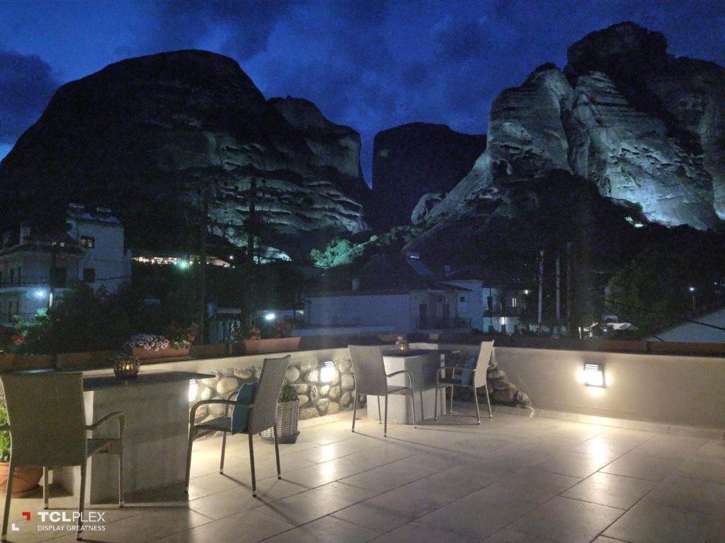 eine Terrasse mit Tischen und Stühlen in der Nacht mit Bergen in der Unterkunft Oikia guesthouse in Kalambaka