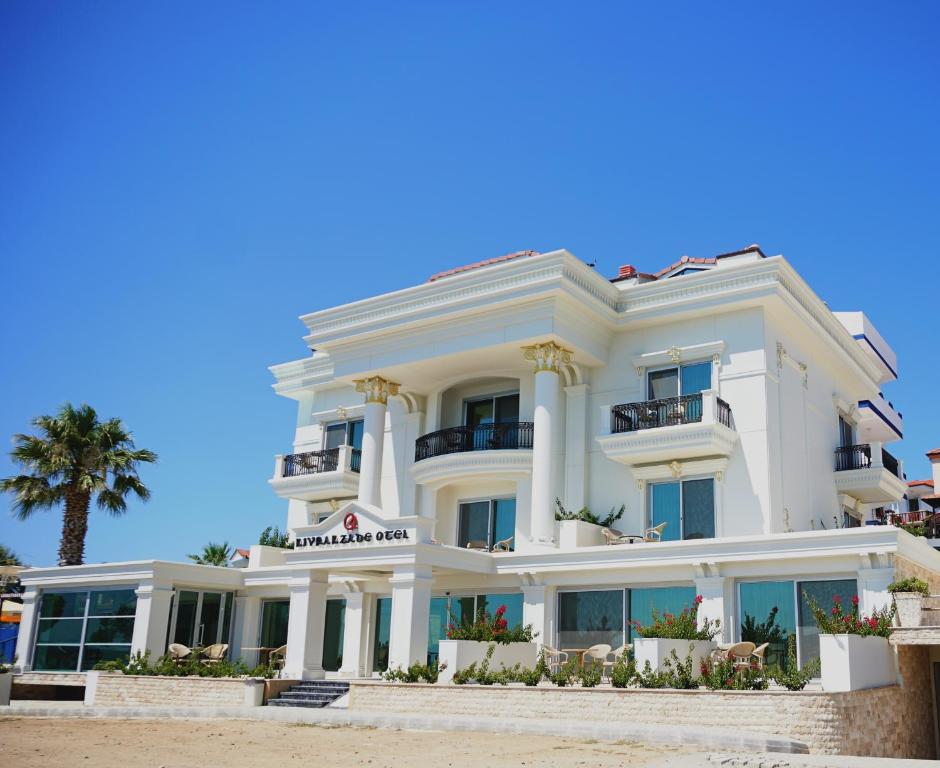 a white building on the beach with a palm tree at Kıvrakzade Otel in Ayvalık