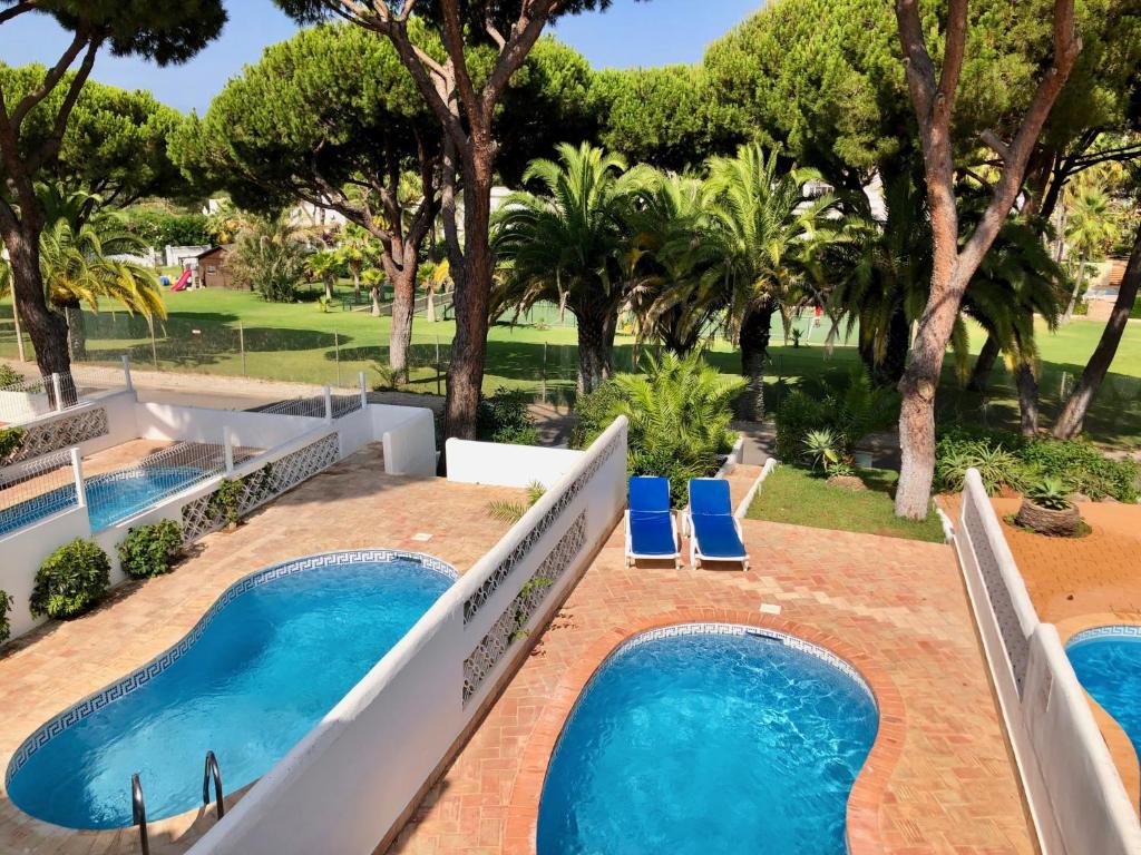 uma vista para duas piscinas com cadeiras azuis e árvores em Vale Do Garrao Villas em Vale do Lobo