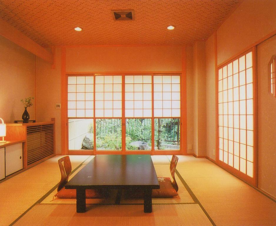 uma sala de jantar com uma mesa e duas janelas em Okumizuma Onsen em Kaizuka