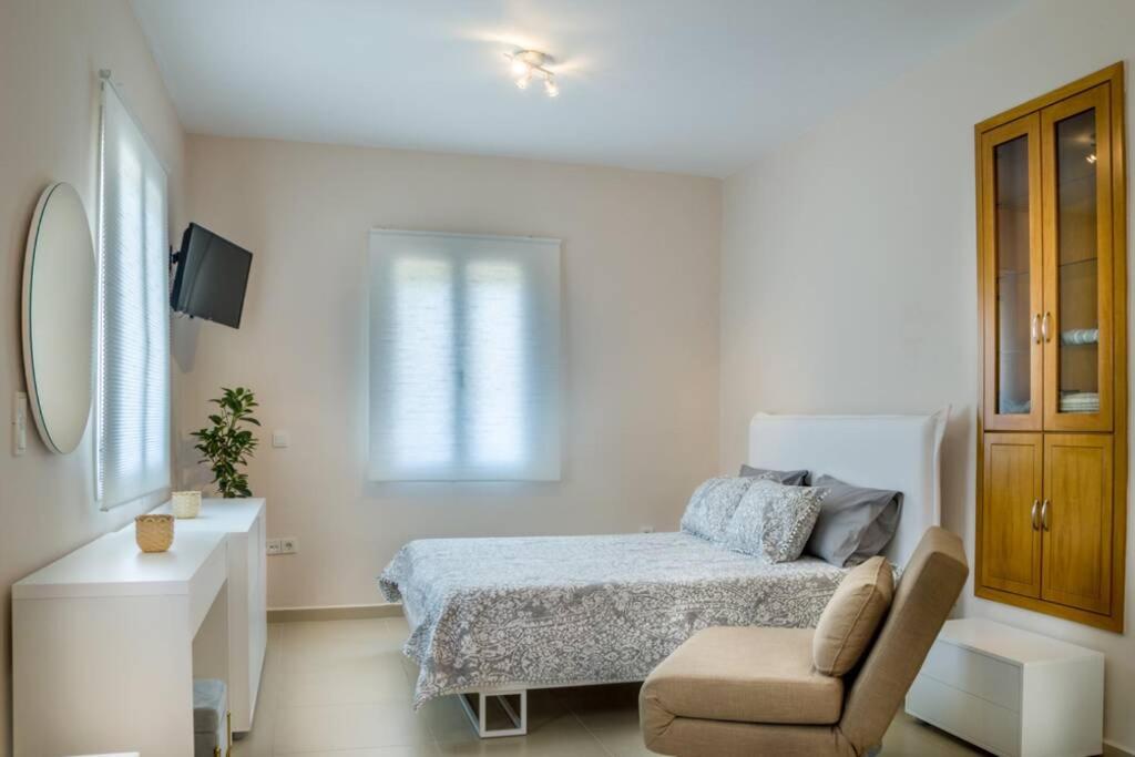 a white bedroom with a bed and a chair at Blanca Serenidad Luxury Apartment in Methana