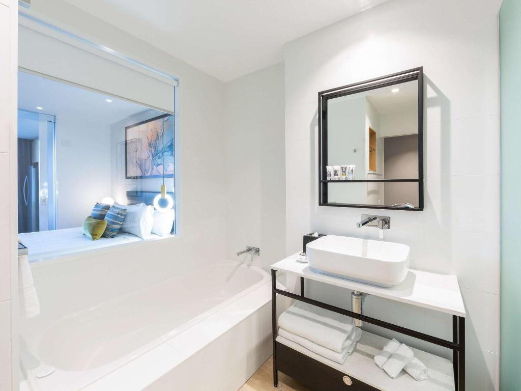 a white bathroom with a sink and a mirror at Mercure Canberra Belconnen in Canberra