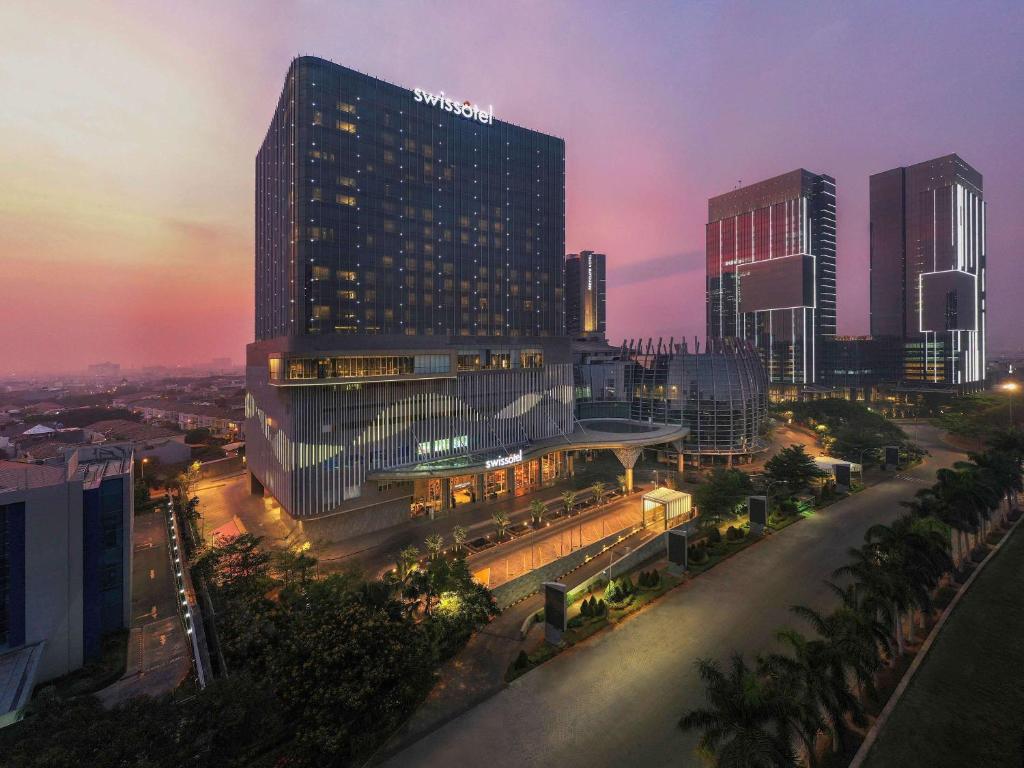 Swissôtel Jakarta PIK Avenue في جاكرتا: أفق المدينة مع مبنى طويل في الليل