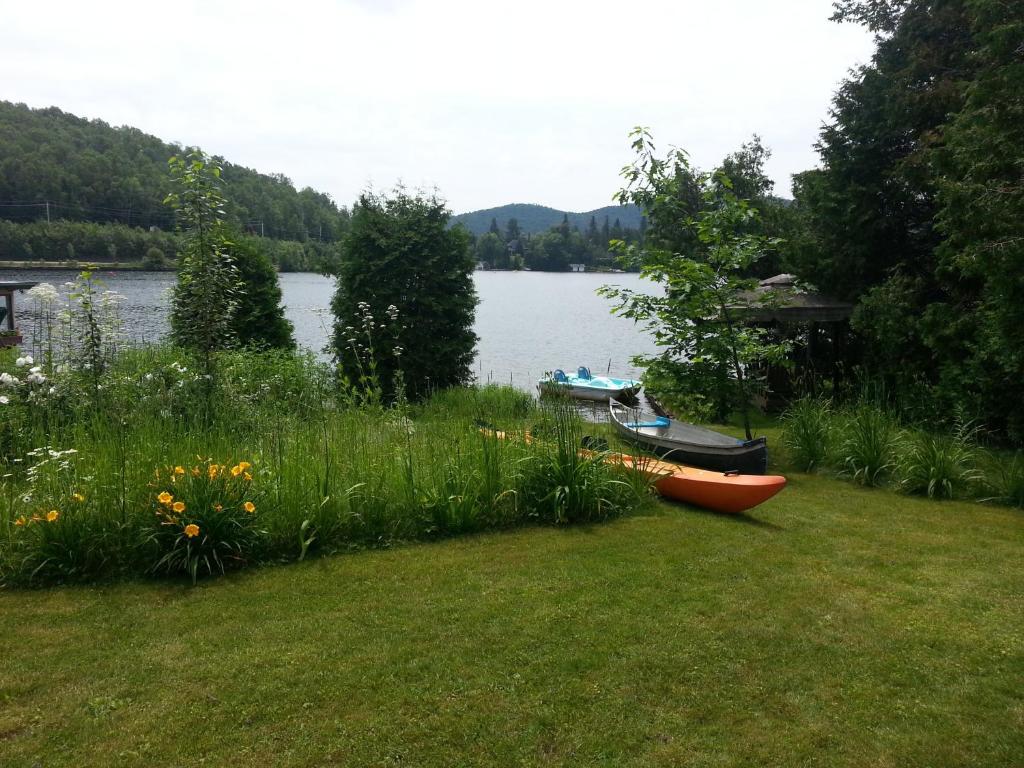 a garden with a boat on the shore of a lake at Auberge Aux Nuits de Rêve in Sainte-Agathe-des-Monts