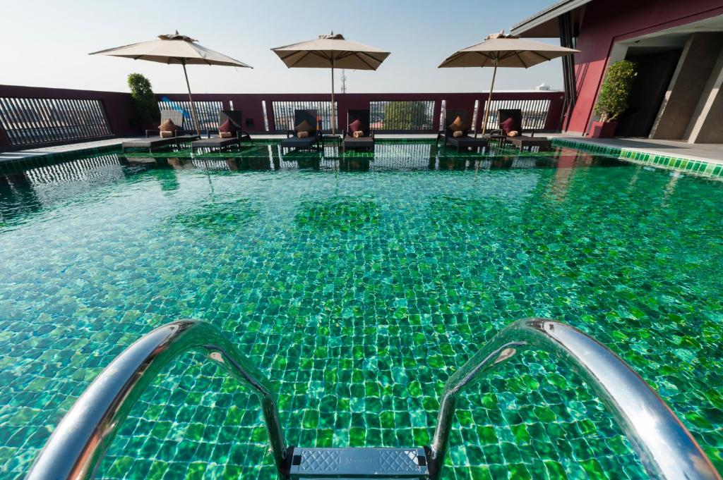 A rooftop pool with a broad tiled deck, umbrellas, and seated guests.