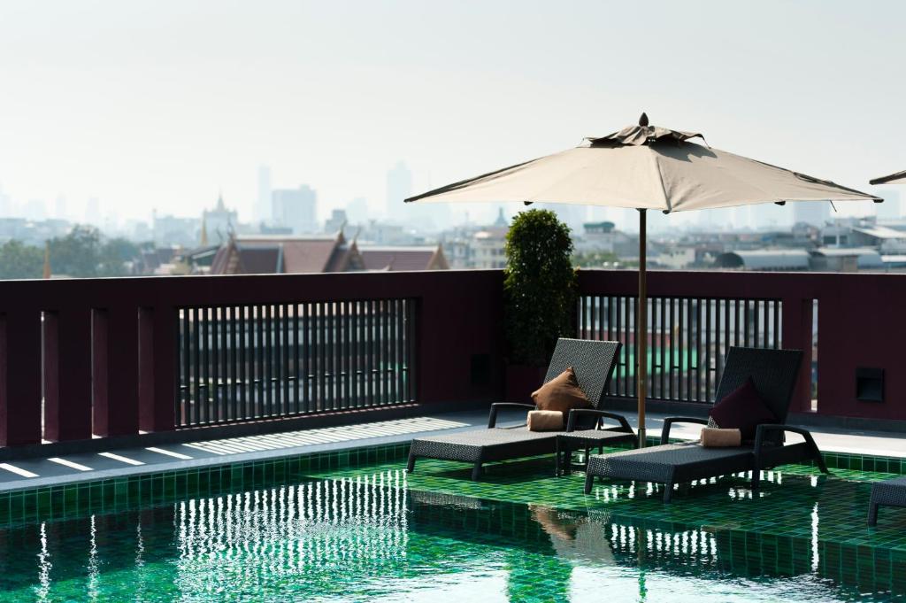 A rooftop poolside view with two loungers, an umbrella, and a distant city skyline.