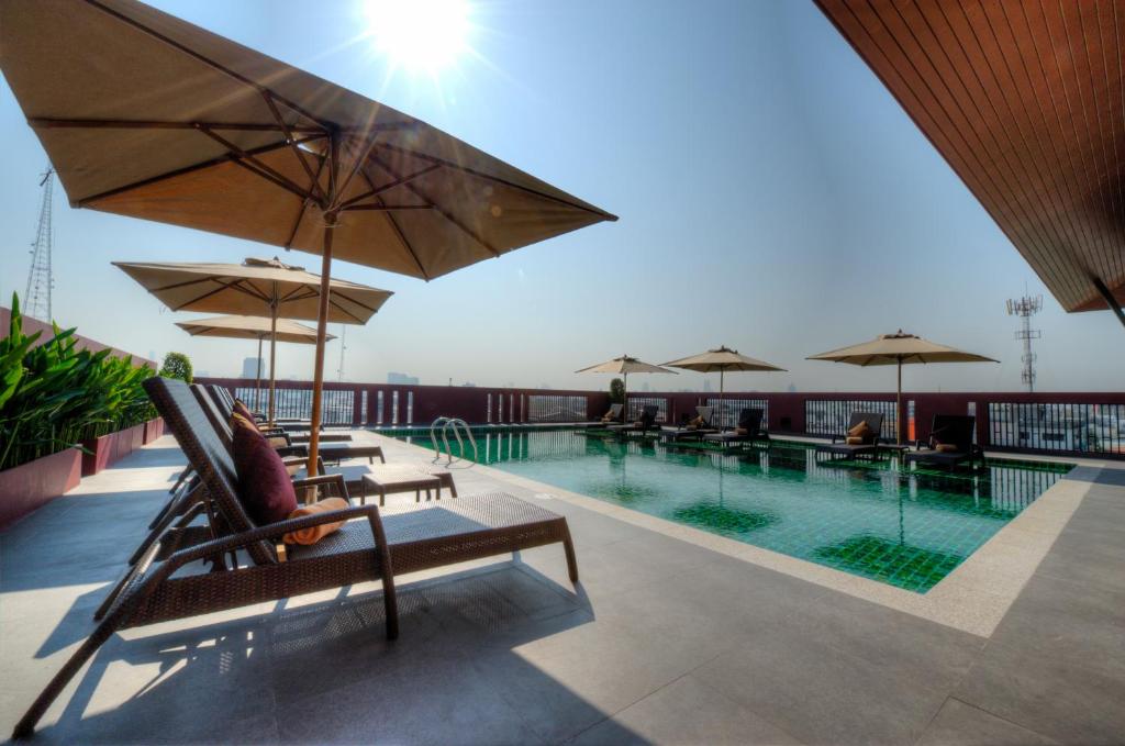 A rooftop pool deck with loungers, umbrellas and bright open sky.