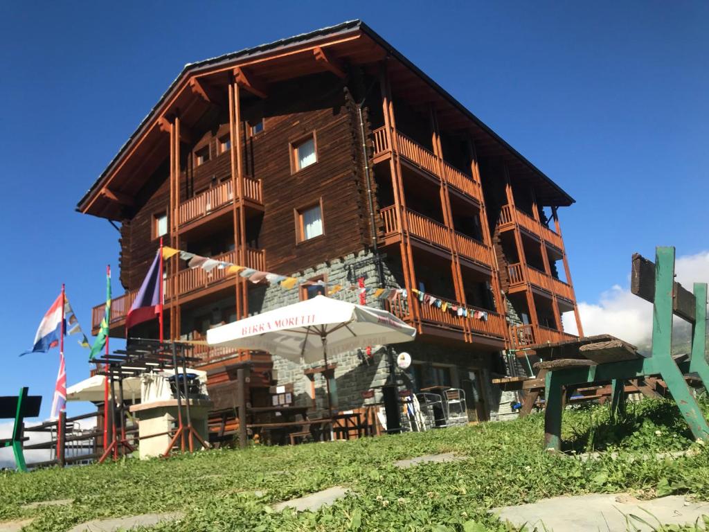 - un grand bâtiment en bois avec un parasol devant dans l'établissement Edelweiss Hotel Champoluc, à Champoluc