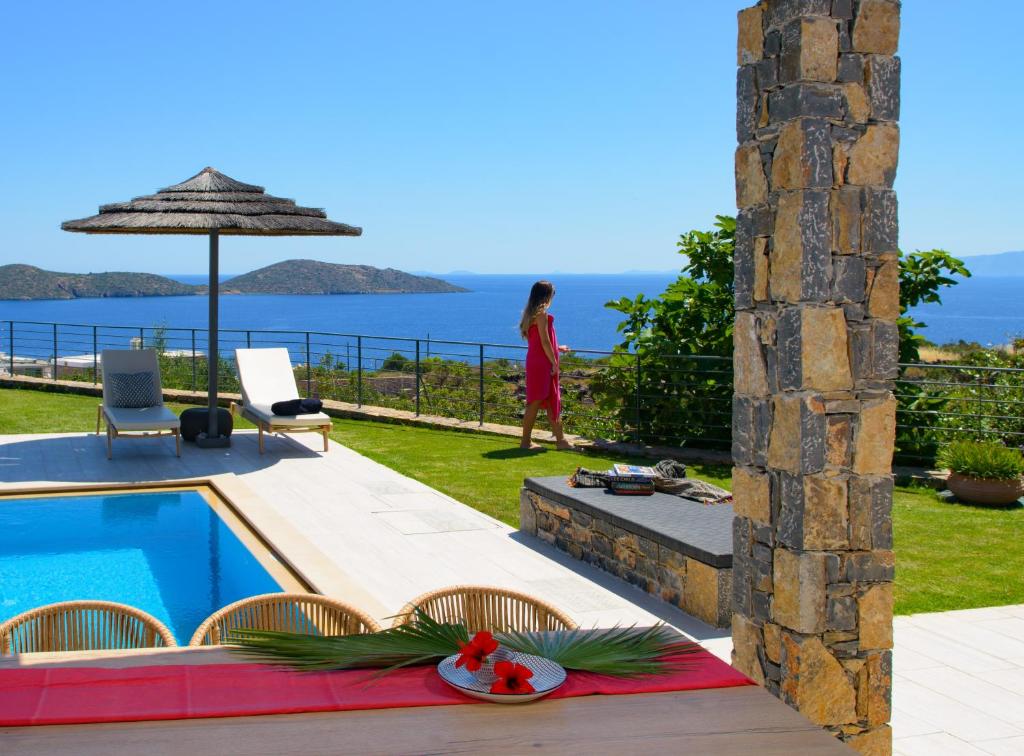 a woman walking by a swimming pool next to a villa at Anemos Elounda Villas in Elounda