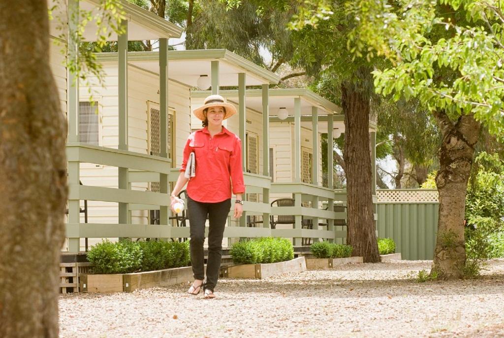 une femme dans un chapeau debout devant un bâtiment dans l'établissement Lake Hamilton Motor Village and Caravan Park, à Hamilton