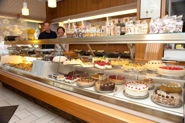 dos personas de pie detrás de un mostrador de panadería con pasteles y pasteles en Hotel Goldinger en Landstuhl
