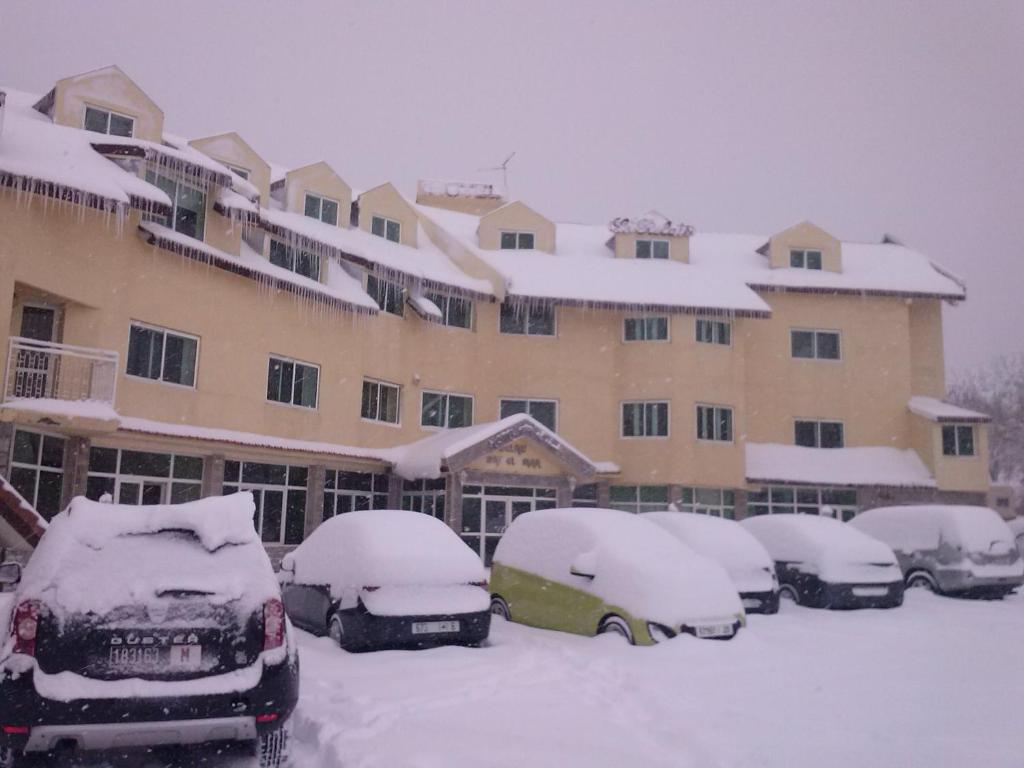 um grupo de carros estacionados num parque de estacionamento coberto de neve em Hôtel Relais Ras El Maa em Ifrane