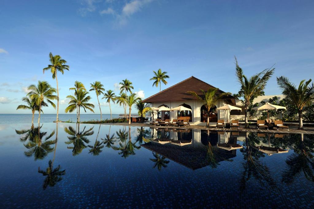 a resort with a swimming pool with palm trees and the ocean at The Residence Zanzibar in Kizimkazi