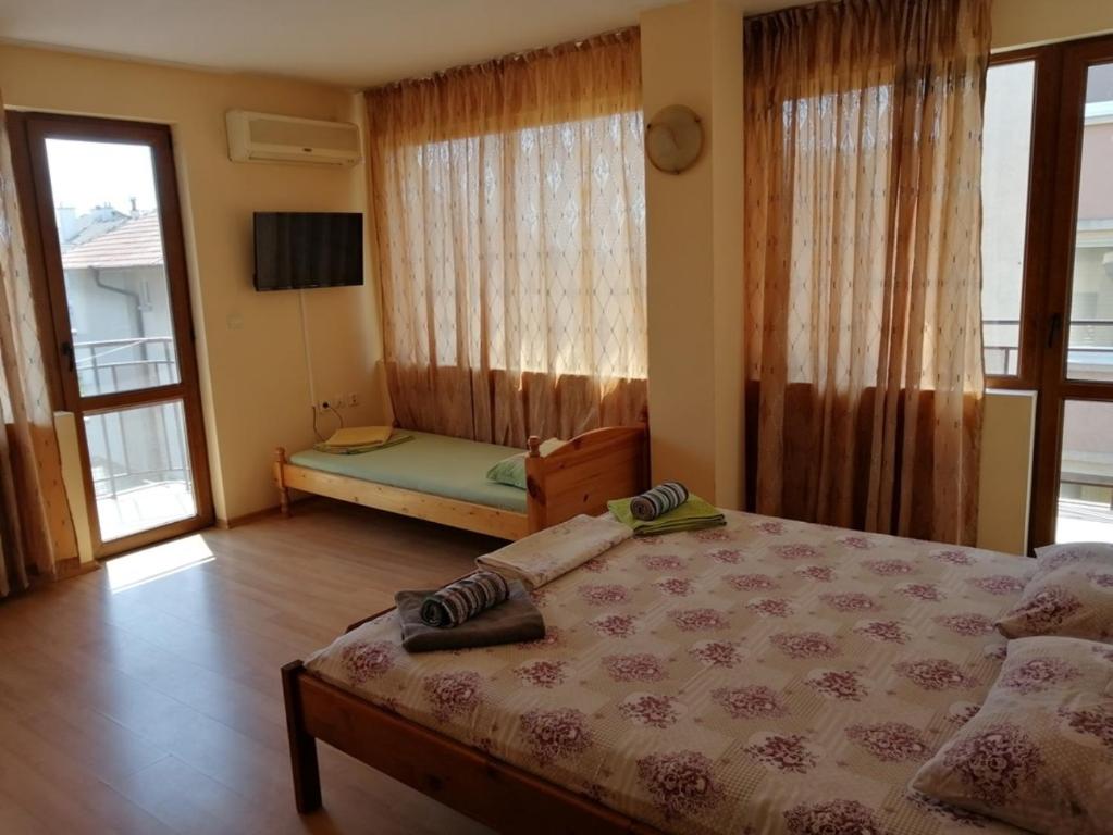 a bedroom with a bed and a tv and windows at Guest House "Zora - Sarafovo" in Burgas