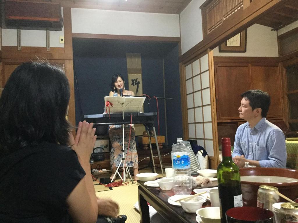 una mujer haciendo una presentación en una habitación con un hombre y una mujer en ゲストハウスやごろう, en Iizuka