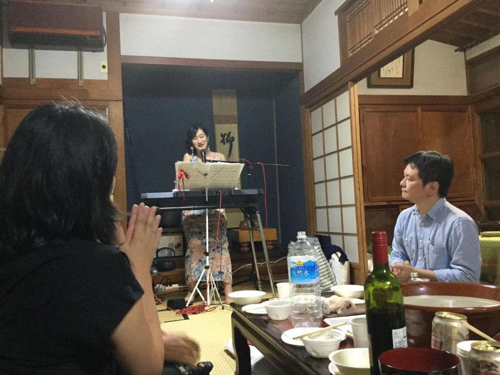 a woman giving a presentation in a room with a man and woman at ゲストハウスやごろう in Iizuka
