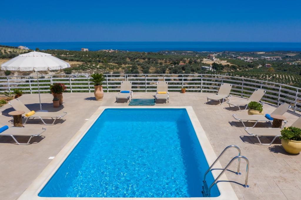 a swimming pool with chairs and a view of the ocean at Haravgi 3 Bedrooms Villa in Agia Triada