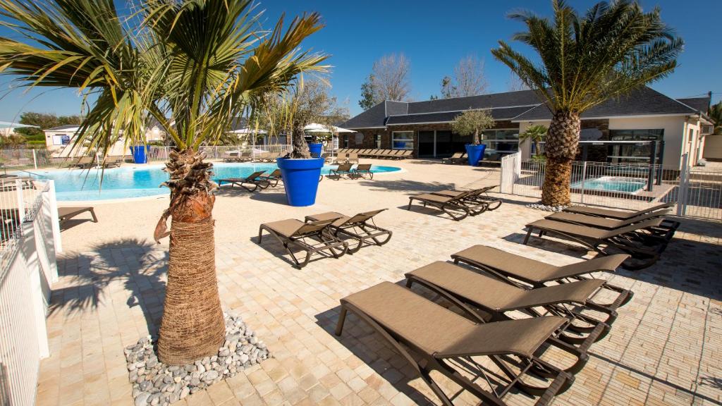 a group of lounge chairs and palm trees next to a pool at M&V Resort Camping in Langrune-sur-Mer