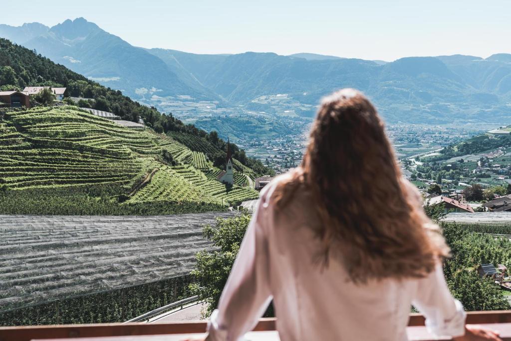 a woman sitting on a ledge looking out at the mountains at Hotel Am Sonneck in Lagundo