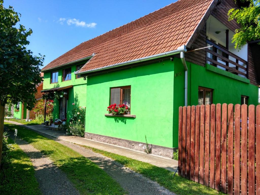 a green house with a red roof and a fence at Csergő Ildikó vendégház in Lăzarea