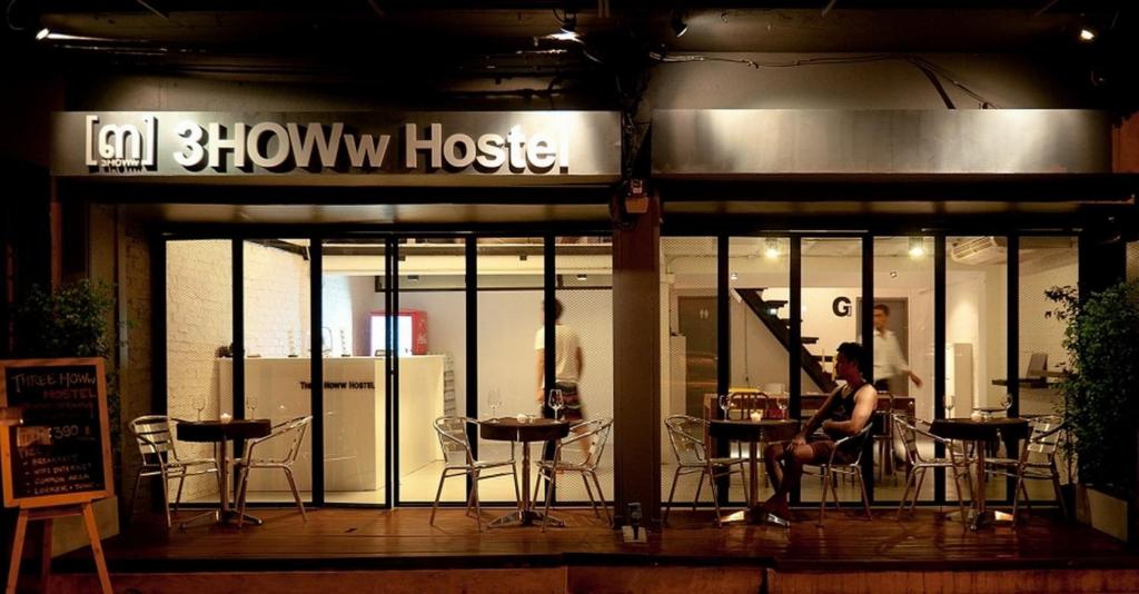 una mujer sentada en una mesa frente a una tienda en 3Howw Hostel Khaosan, en Bangkok