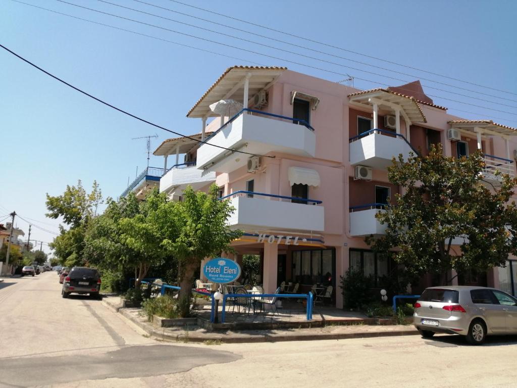 un edificio rosa con coches estacionados frente a él en Hotel Eleni en Paralia Dionysiou