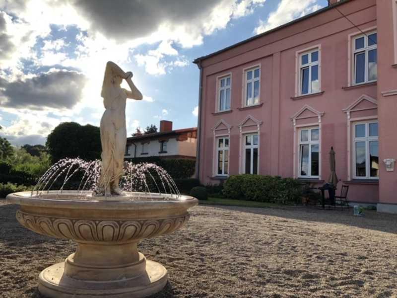 a statue in front of a fountain in front of a pink building at Schlosshotel Gross Koethel in Hohen Demzin