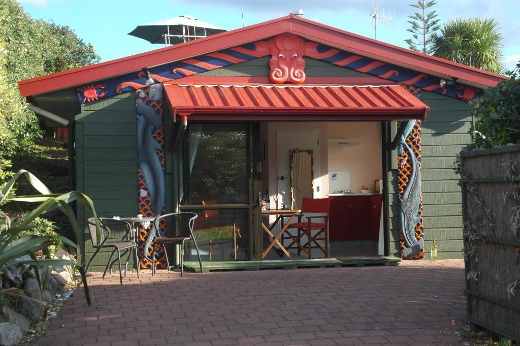um barracão verde com um telhado vermelho e um pátio em Moanarua Beach Cottage em Ohope Beach