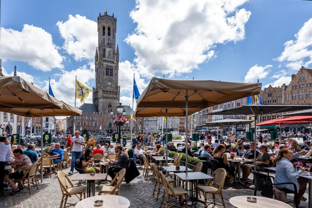 a group of people sitting at tables in a city with a clock tower at Hotel Central in Bruges