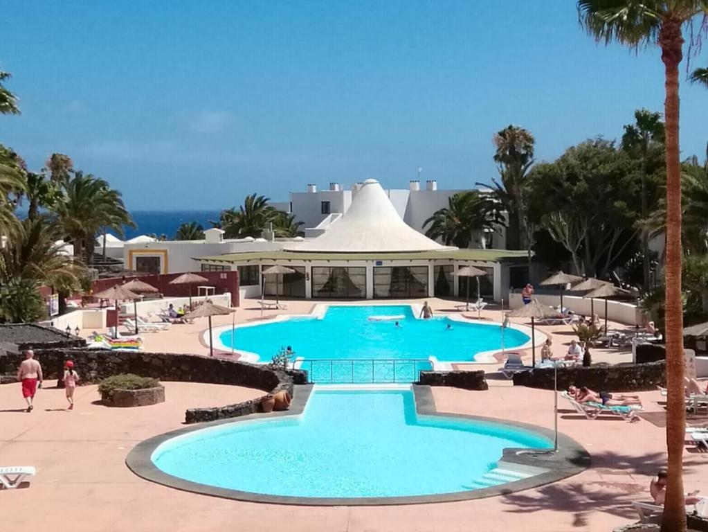 uma piscina num resort com pessoas a passear em PLAYA ROCA MODERN STUDIO - Seafront Pool Complex em Costa Teguise