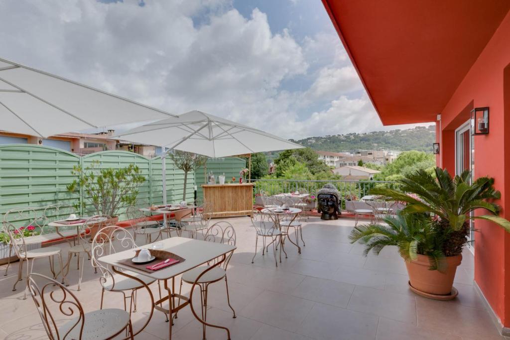 un patio con mesas, sillas y una sombrilla en Hôtel CasaBella en Mouans-Sartoux