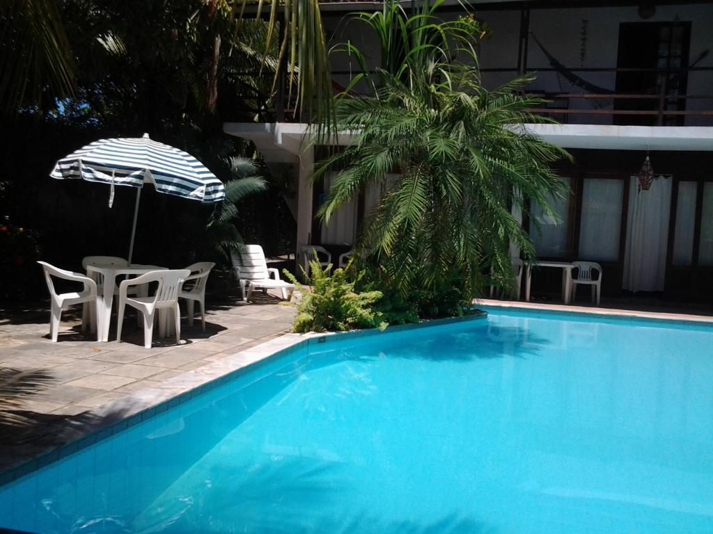 a blue swimming pool with chairs and an umbrella at Exclusive Guest House in Porto De Galinhas