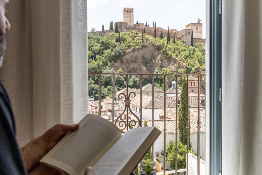 a man reading a book in front of a window at INOLVIDABLES VISTAS A LA ALHAMBRA, Parking in Granada