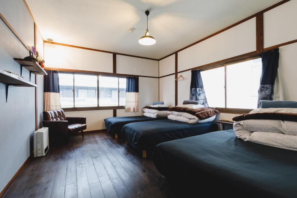 una camera con due letti e una sedia e finestre di Couch Potato Hostel - Vacation STAY 88243 a Matsumoto