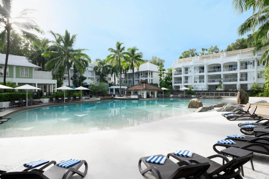 a hotel room with a pool, chairs, and tables at Peppers Beach Club & Spa in Palm Cove