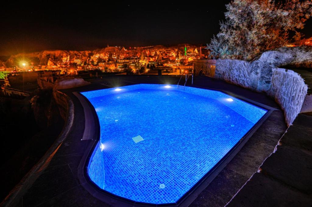a swimming pool at night with a city in the background at Cappadocia Caves Hotel in Göreme