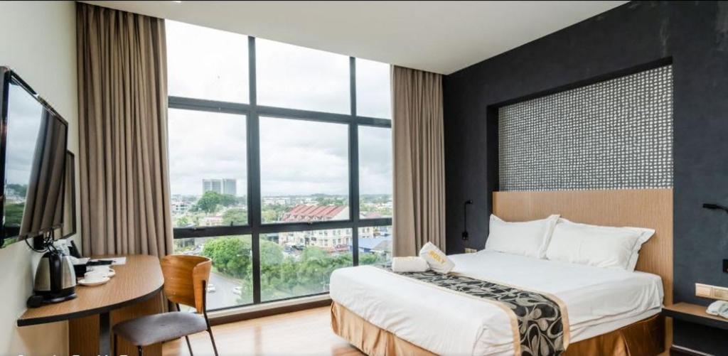 Schlafzimmer mit einem Bett, einem Schreibtisch und einem großen Fenster in der Unterkunft Roxy Hotel & Apartments in Kuching