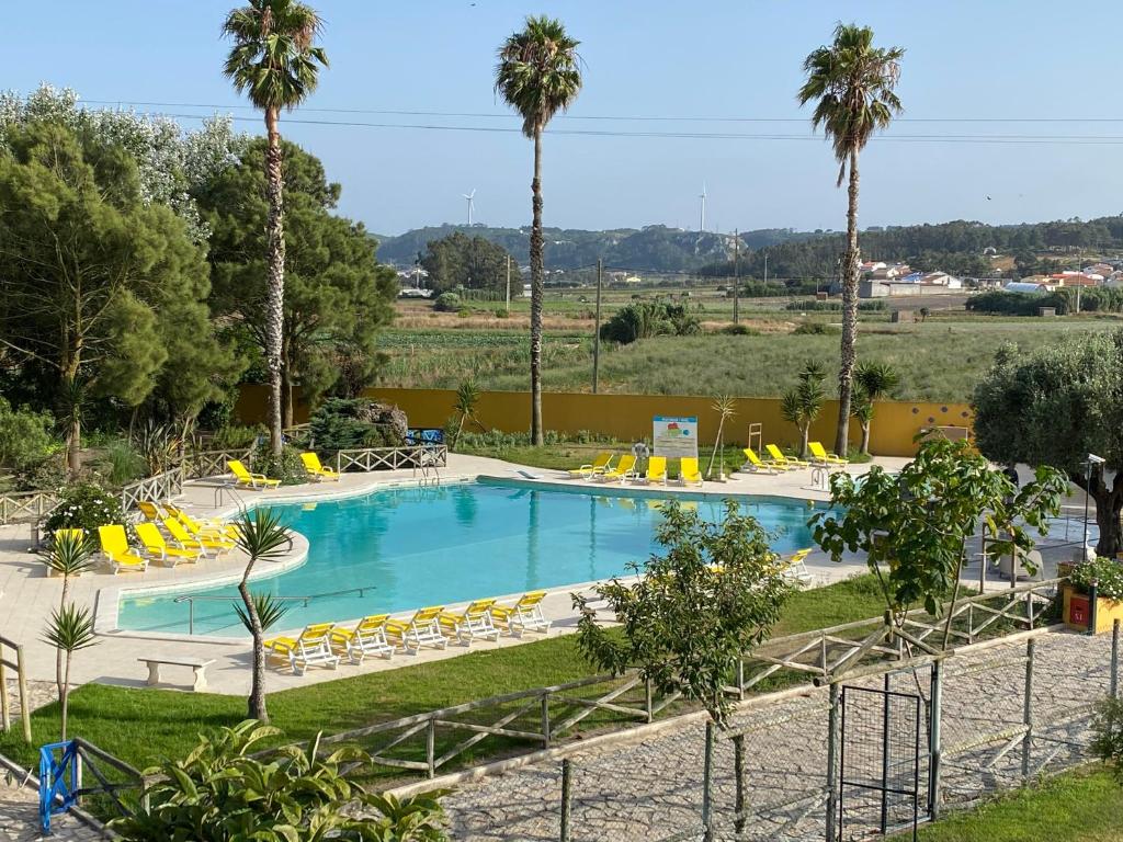 a large swimming pool with yellow chairs and palm trees at Charm Azenha DÓbidos Farm in Olho Marinho
