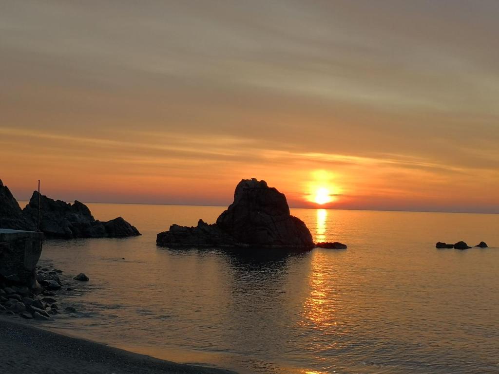 una puesta de sol en una playa con una roca en el agua en appartamento in villa a Pietragrande, en Stalettì
