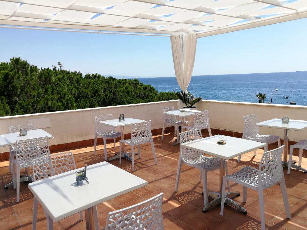 a restaurant with white tables and chairs and the ocean at B&B Il Mare degli Dei in Letojanni